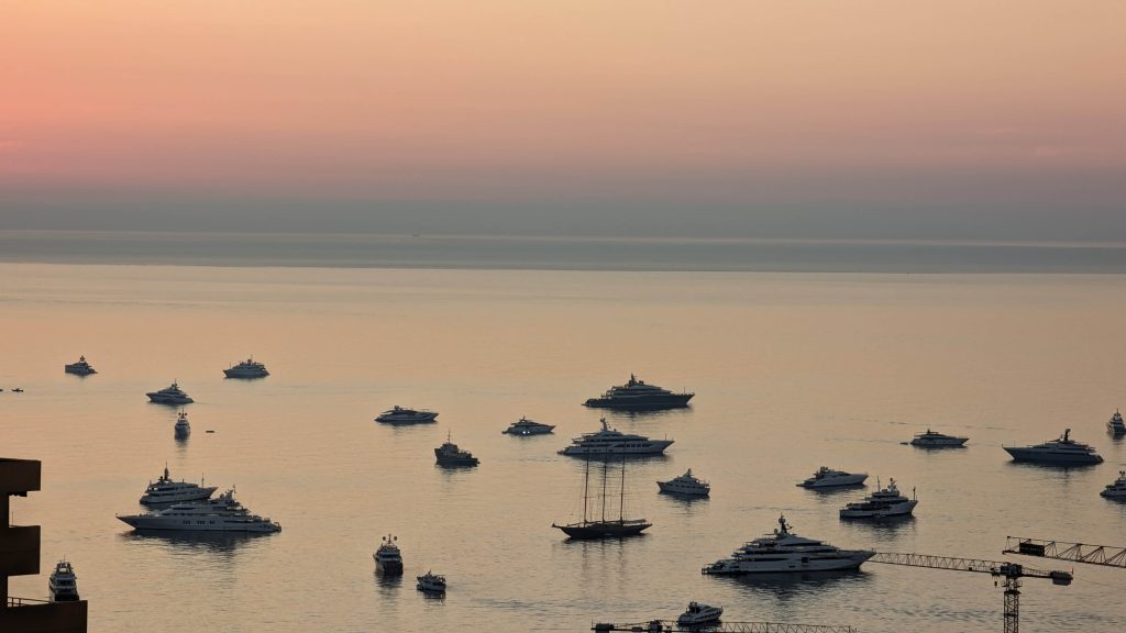 yachts of different sizes on the water under an orange sunset sky during monaco yacht show 2023