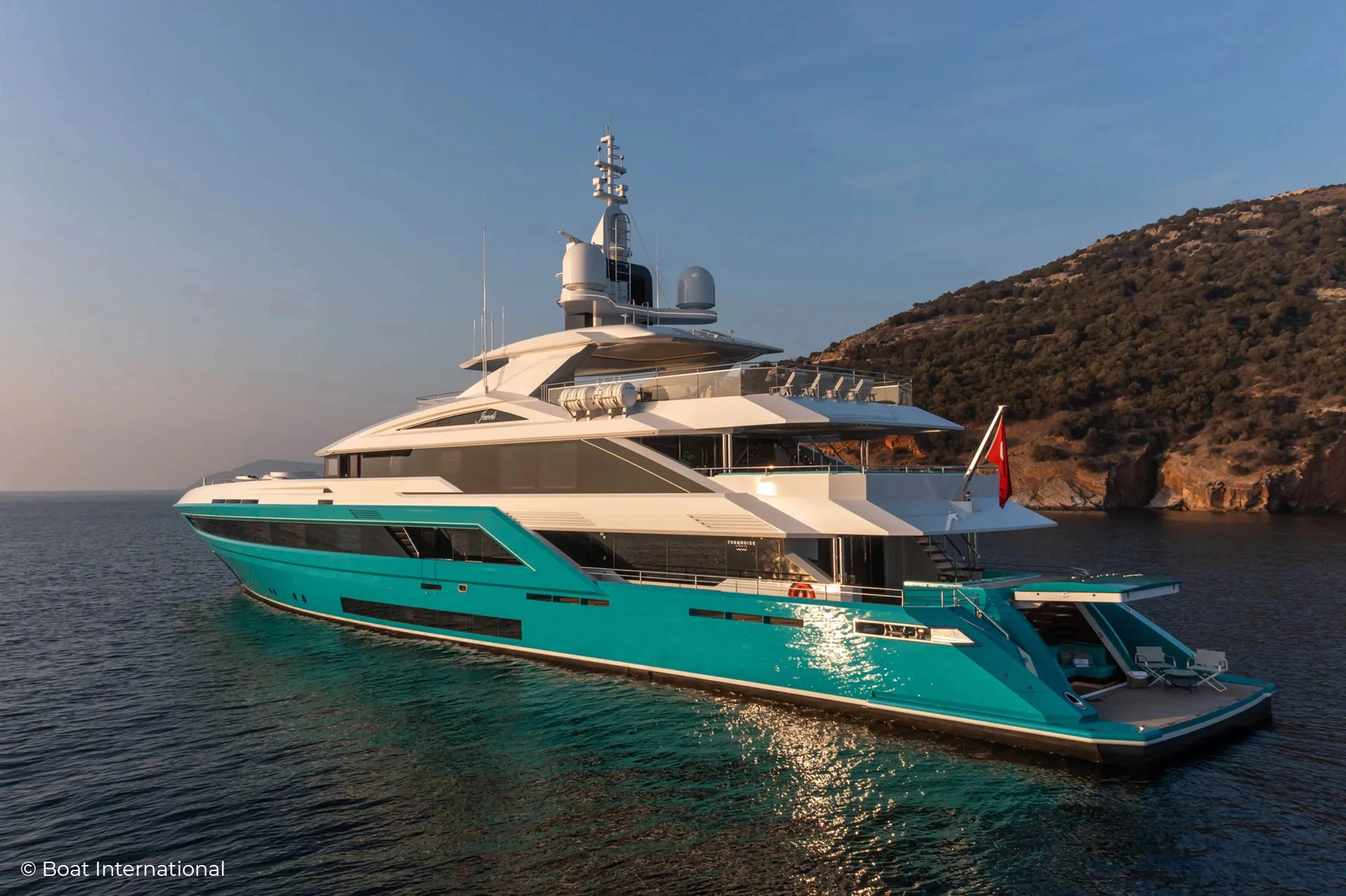 Turquoise shipyard's superyacht Jewel with its vivid turquoise blue hull lit by the sun. Illuminated Yacht Sign from Lumenautica.